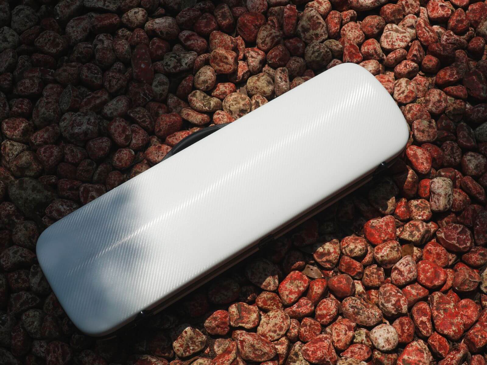 White Molto Classic oblong violin case resting on rocks